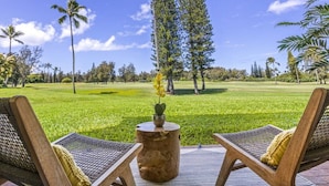 A view from a lounge area with two wicker chairs, a small round table with a plant, and a golf course in the background. - Spacious Condo on Turtle Bay Golf Course (Kahuku)