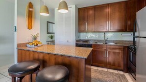 A kitchen with wooden cabinets, a granite countertop, a built-in oven, and two pendant lights. - Spacious Condo on Turtle Bay Golf Course (Kahuku)
