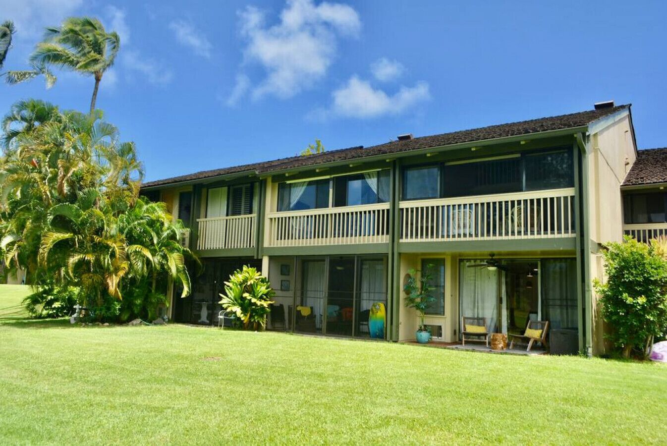 A two-story motel with a balcony on the second floor, surrounded by palm trees and a well-maintained lawn.