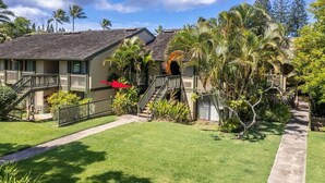 A two-story house with a covered porch, a staircase, and a well-maintained lawn. - Spacious Condo on Turtle Bay Golf Course (Kahuku)