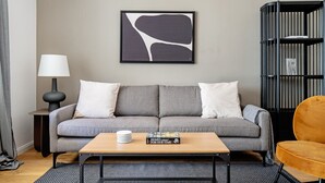 A living room with a grey sofa, a coffee table with a book, a lamp, and a black bookshelf. - Lovely Leopoldstadt 2BR w/ Elevator & city view, nr Danube, by Blueground (Vienna)