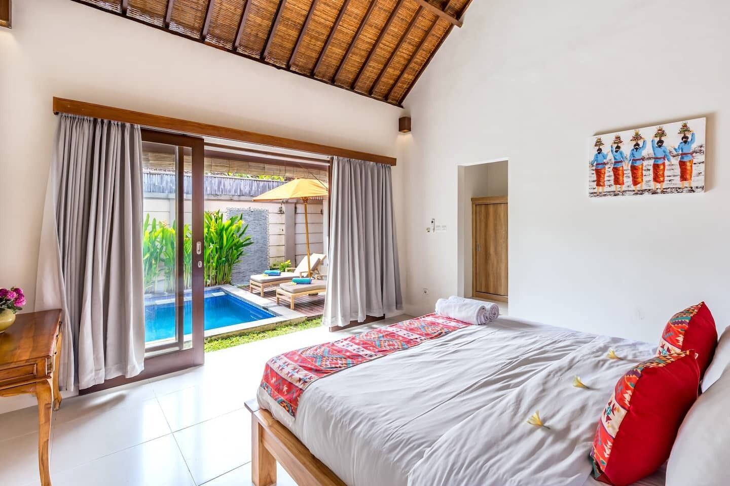A bedroom with a large bed, a view of a swimming pool, and a door leading to an outdoor area.