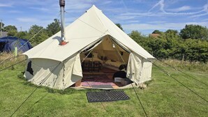Een koepelvormige tent met schoorsteen, opgesteld op een grasveld met bomen op de achtergrond.