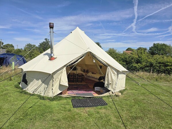 A dome-shaped tent with a chimney, set up on a grassy field with trees in the background.