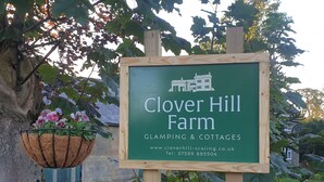 Une pancarte indiquant le nom de la ferme Clover Hill et faisant la publicité de locations de logements insolites et de chalets, avec un numéro de téléphone et une adresse de site web.