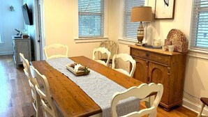 Un comedor con mesa de madera, sillas blancas, una lámpara y un objeto decorativo en un mueble.