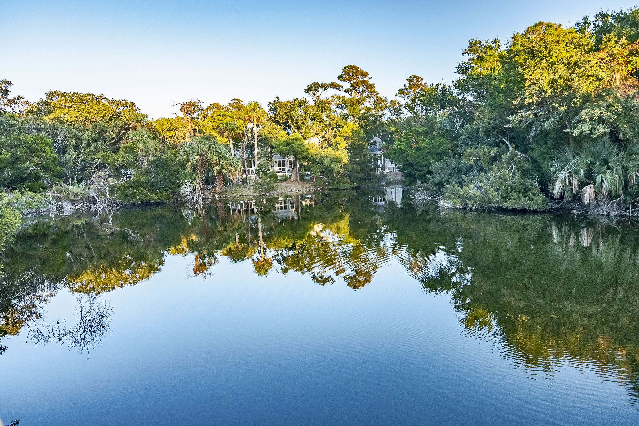 Un lac paisible où se reflètent les arbres et une maison.