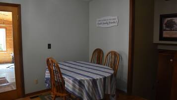A dining area with a table covered by a striped tablecloth, two wooden chairs, and a sign on the wall.