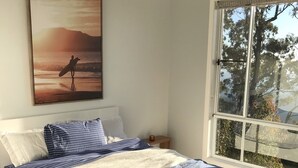 A bedroom with a bed, a ceiling fan, a window with a view of trees, and a painting on the wall. - Views from Stradbroke to Tweed Heads (Wongawallan)