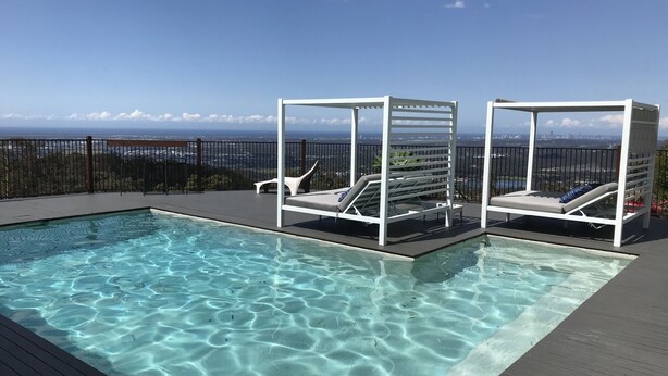 A clear swimming pool with two white sun loungers and a view of the city skyline. - Views from Stradbroke to Tweed Heads (Wongawallan)