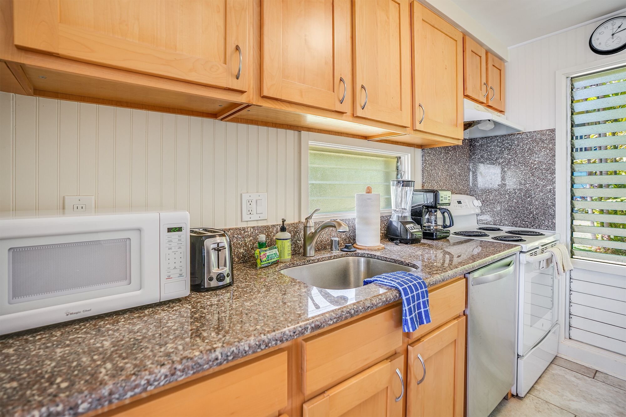 A kitchen with wooden cabinets, a microwave, a toaster, a sink, a coffee maker, and a stove.