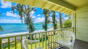 Ein Balkon mit zwei weißen Plastikstühlen, einem Glastisch und Blick auf den Ozean und den Strand.