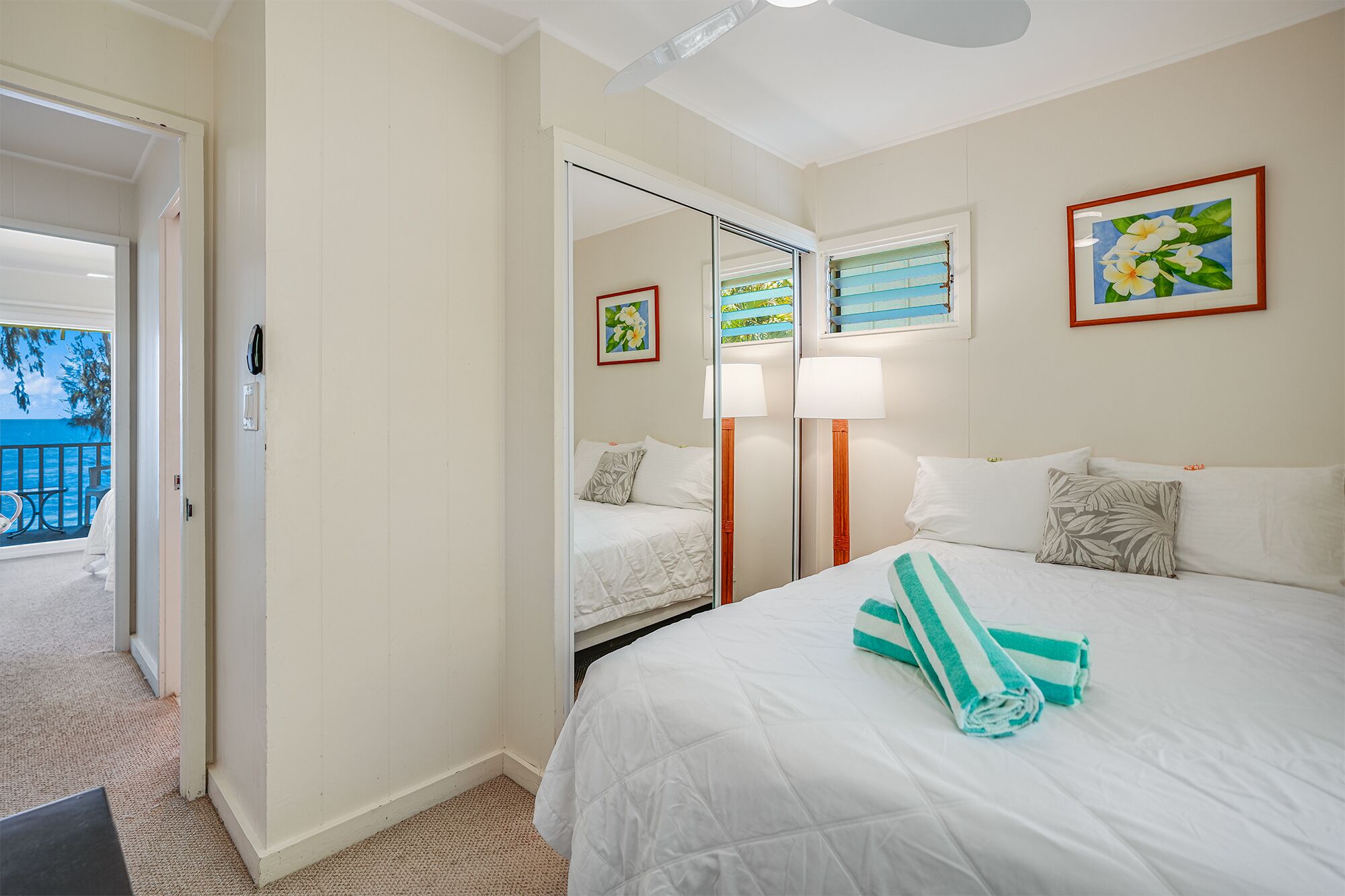 Habitación de hotel con cama, espejo, ventana con vista al mar y puerta que da a un balcón.