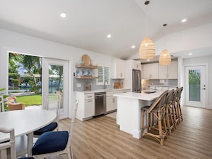 A modern kitchen with white cabinets, a central island, and a dining area with wicker chairs.