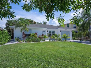 A two-story house with a well-maintained lawn, surrounded by various plants and trees.
