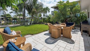 Eine Terrasse im Freien mit Korbmöbeln, einem Grill und einem Pool im Hintergrund.