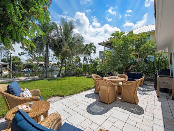 An outdoor patio with wicker furniture, a grill, and a pool in the background.