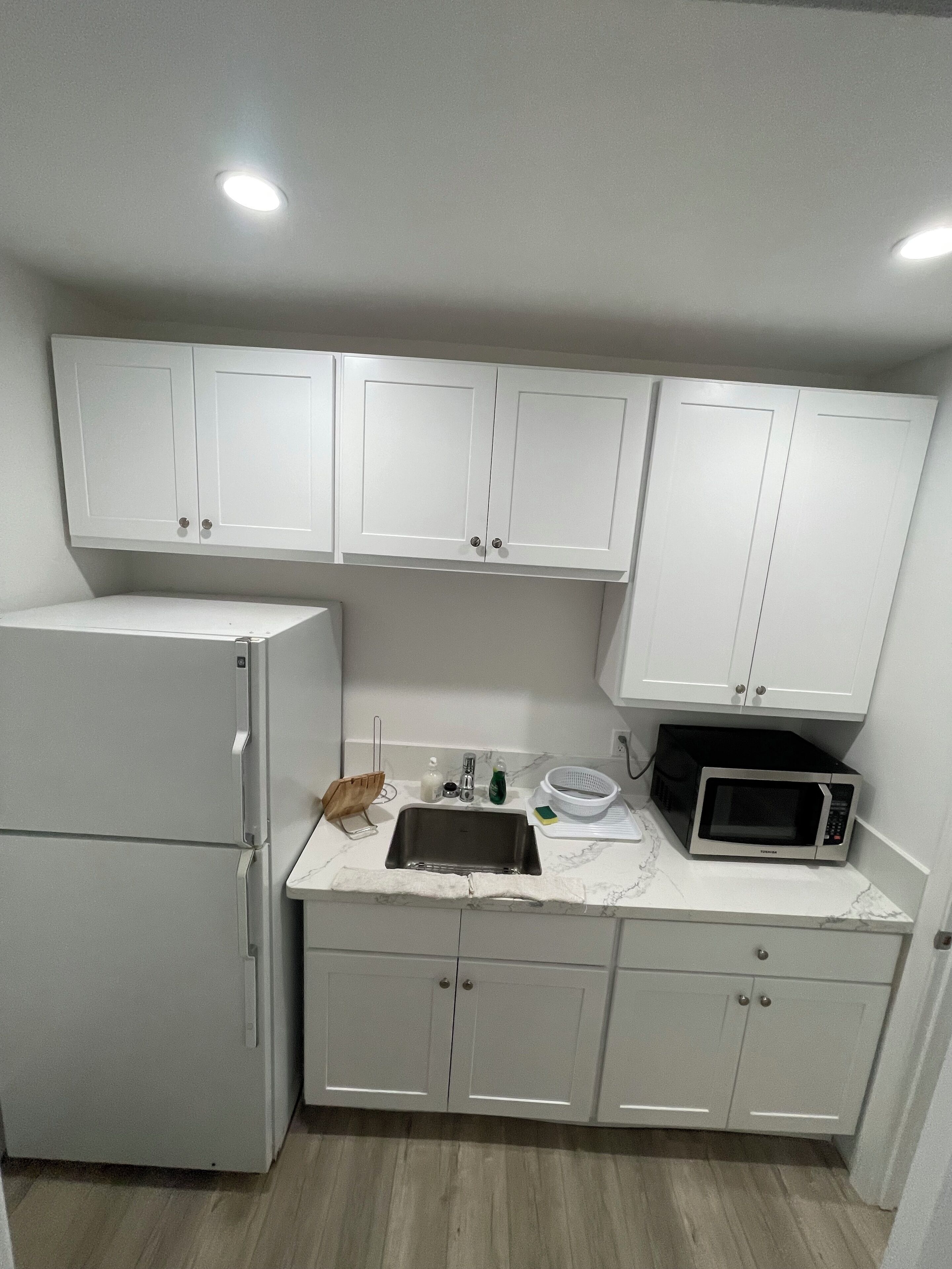 A compact kitchen with white cabinets, a refrigerator, a sink, and a microwave.