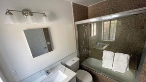 Ein Badezimmer mit weißem Waschbecken, Toilette, einer Duschkabine und einem Spiegel über dem Waschbecken.