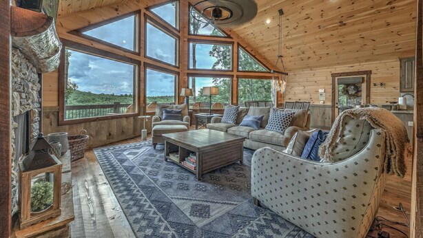 A cozy log cabin interior with a large window, a fireplace, and a comfortable seating area. - Songbird Ridge - Aska Adventure Area | Panoramic Views | Hot Tub | Outdoor Fireplace (Blue Ridge)
