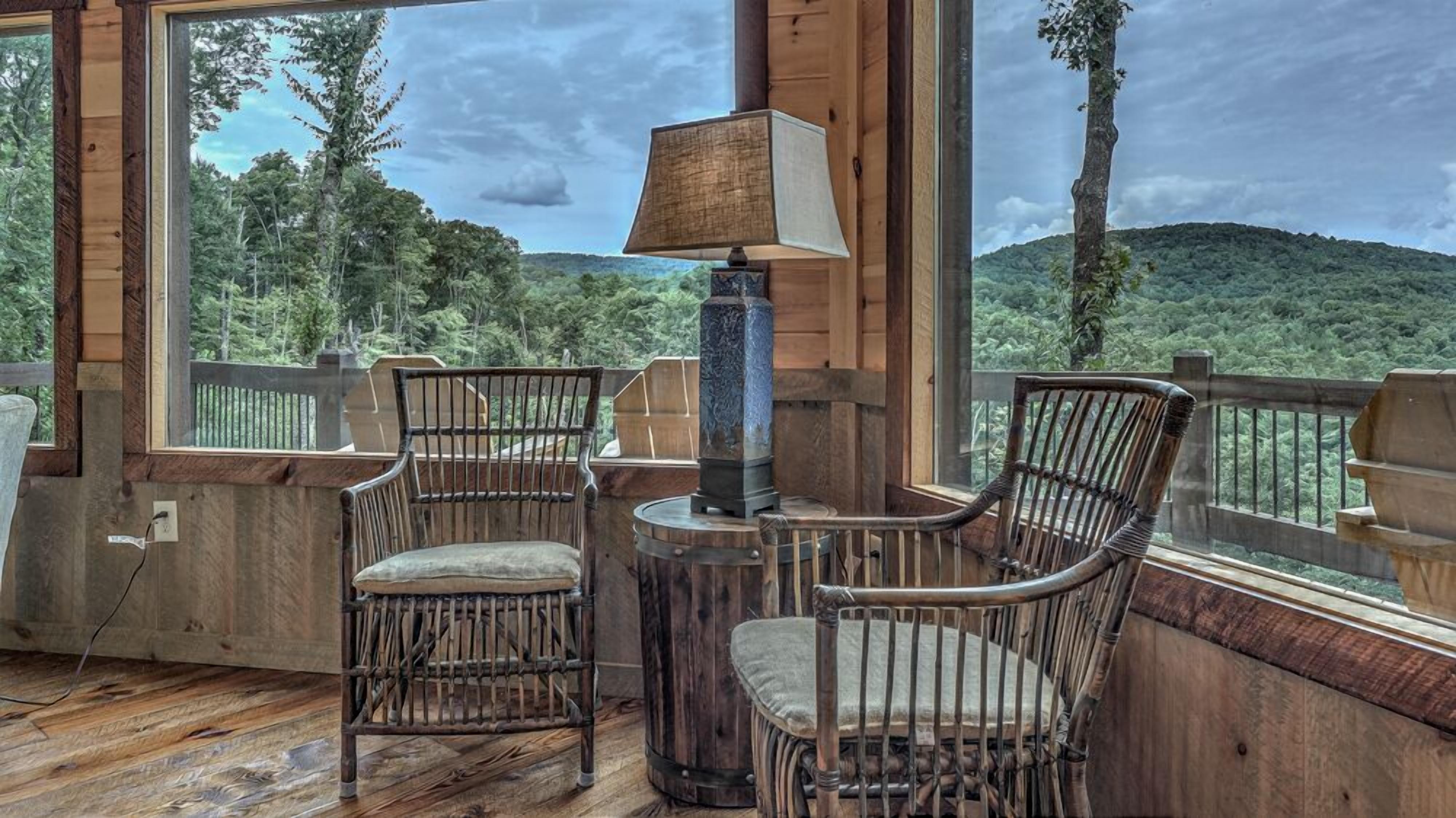 A wooden deck with two wicker chairs and a table, overlooking a forested landscape.