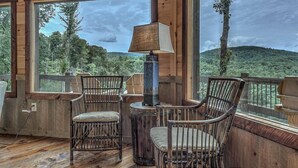 A wooden deck with two wicker chairs and a table, overlooking a forested landscape. - Songbird Ridge - Aska Adventure Area | Panoramic Views | Hot Tub | Outdoor Fireplace (Blue Ridge)
