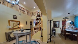 A spacious living area with a dining table, a staircase with a Christmas tree, and a large mirror on the wall.