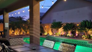 An outdoor patio with a pool, surrounded by palm trees and string lights.