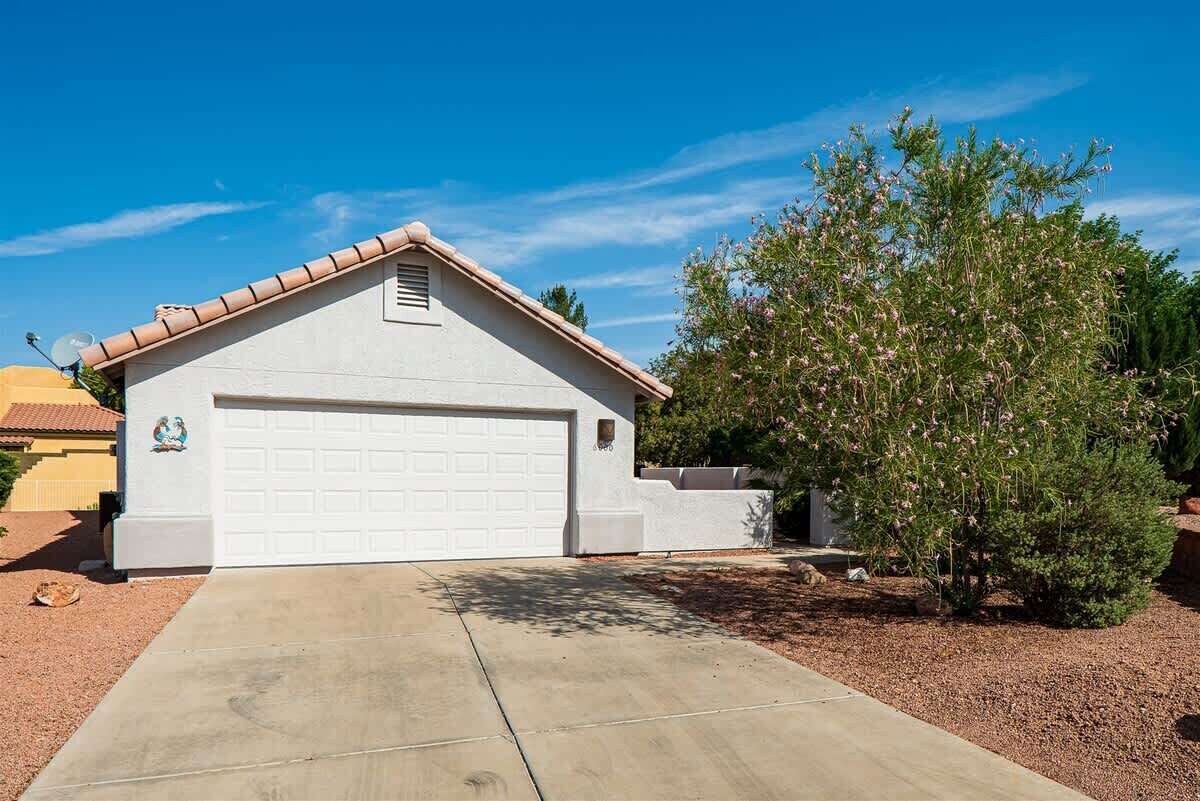 A single-story house with a white garage door, a small attached shed, and a well-maintained garden with a flowering tree.