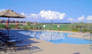 Piscina com espreguiçadeiras e guarda-sóis, cercada por uma vedação e um céu claro.