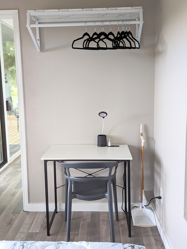 A small room with a white table, a grey chair, a white shelf with black hangers, and a white floor lamp. - The Cozy Container, Country Living, Modern Design (New Waverly)