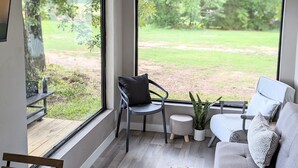 Una sala de estar moderna con ventanas amplias, un sofá gris, una mesita redonda y una planta en maceta.