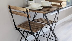 Una mesa de madera con patas metálicas y sillas a juego, junto con una pequeña planta en maceta y un cuenco blanco.