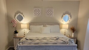 Un dormitorio con una cama, dos mesitas de noche, un ventilador de techo y espejos decorativos en la pared.