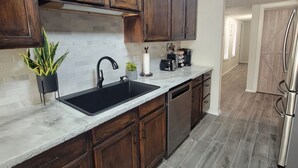 Una cocina con armarios de madera oscura, un lavamanos negro y un refrigerador de acero inoxidable.