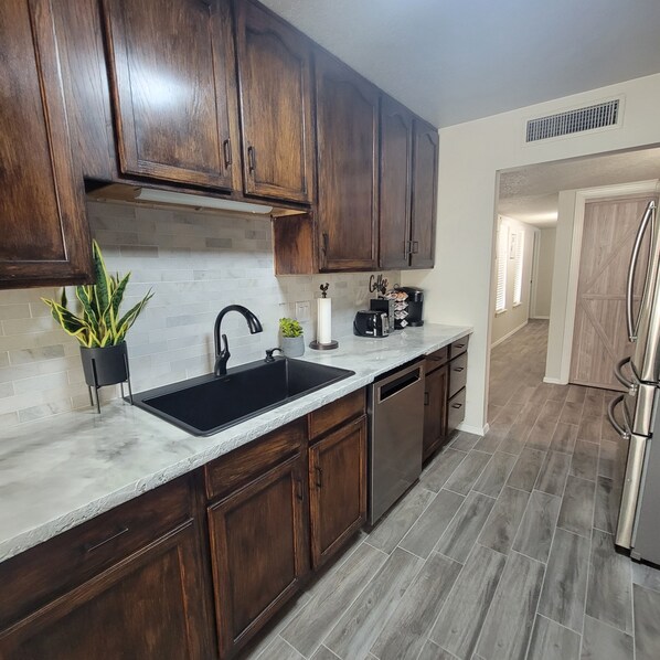 A kitchen with dark wooden cabinets, a black sink, and a stainless steel refrigerator.