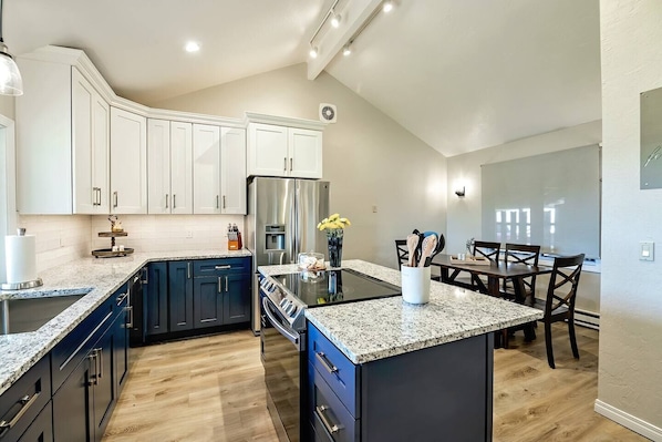 A modern kitchen with dark blue cabinets, a stainless steel refrigerator, and a dining area with a table and chairs.