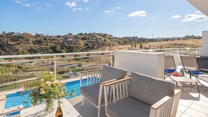 Un balcon avec une piscine, un espace salon extérieur et une vue sur une colline.