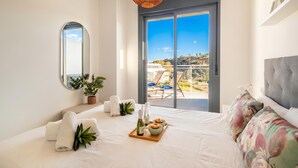 Une chambre à coucher avec un lit, une grande fenêtre, un miroir, une plante et un plateau contenant des bouteilles et des bols.