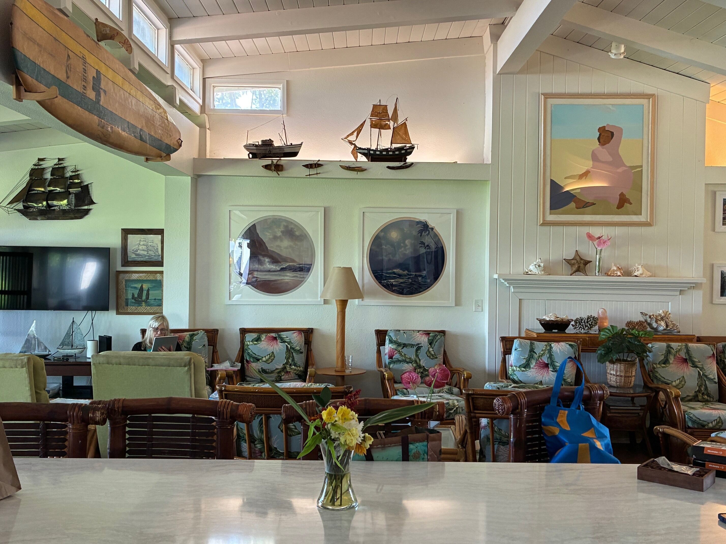 A spacious room with a high ceiling, nautical-themed decor including model ships, framed seascapes, and a fireplace.