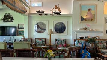 A spacious room with a high ceiling, nautical-themed decor including model ships, framed seascapes, and a fireplace.
