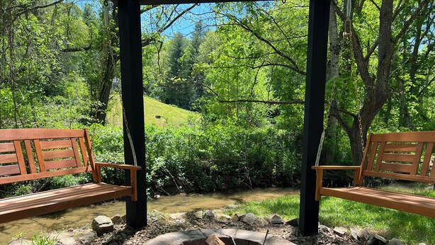 A wooden bench under a pergola overlooking a natural landscape with a stone fire pit.