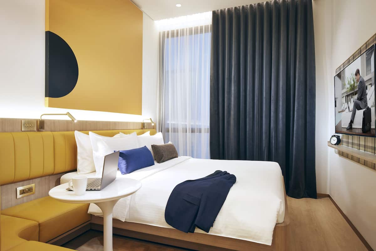 Ein Hotelzimmer mit Bett, kleinem Tisch, einer Couch und einem Fernseher an der Wand.