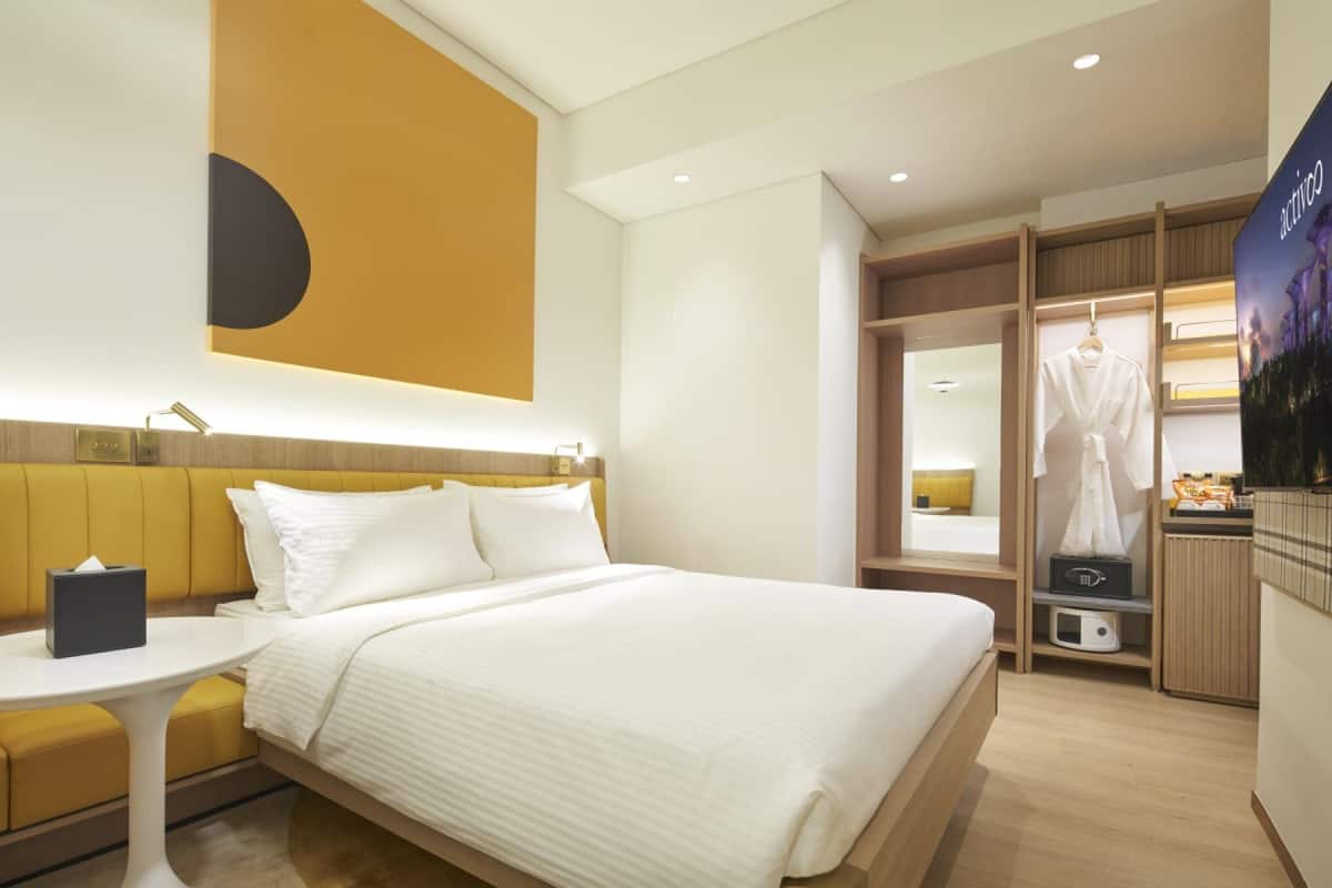 Ein modernes Hotelzimmer mit einem großen Bett, einem Nachttisch, einem kleinen Tisch und einem Kleiderschrank.