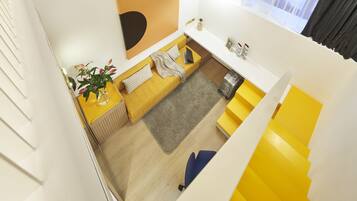 Un intérieur moderne avec un canapé jaune, une petite table agrémentée d’une plante et un escalier dont les marches sont jaunes.