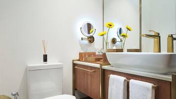 Un baño moderno con lavamanos blanco, detalles dorados y un espejo grande.