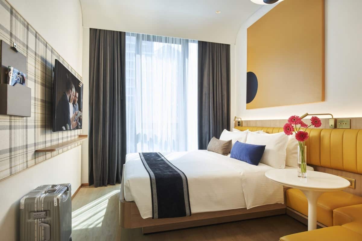 Ein Hotelzimmer mit Bett, Sofa, kleinem Tisch, Fernseher und einem Fenster mit Vorhängen.