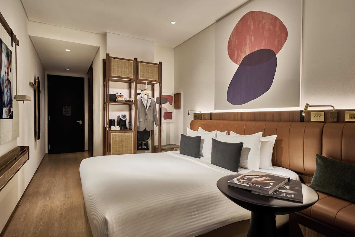 Ein modernes Hotelzimmer mit einem großen Bett, einer Sitzecke mit einer braunen Ledersofa, einem kleinen Tisch und einem an der Wand montierten Regal mit persönlichen Gegenständen.