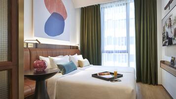 A hotel room with a large bed, a bedside table with a vase, and a view of the city through the window.