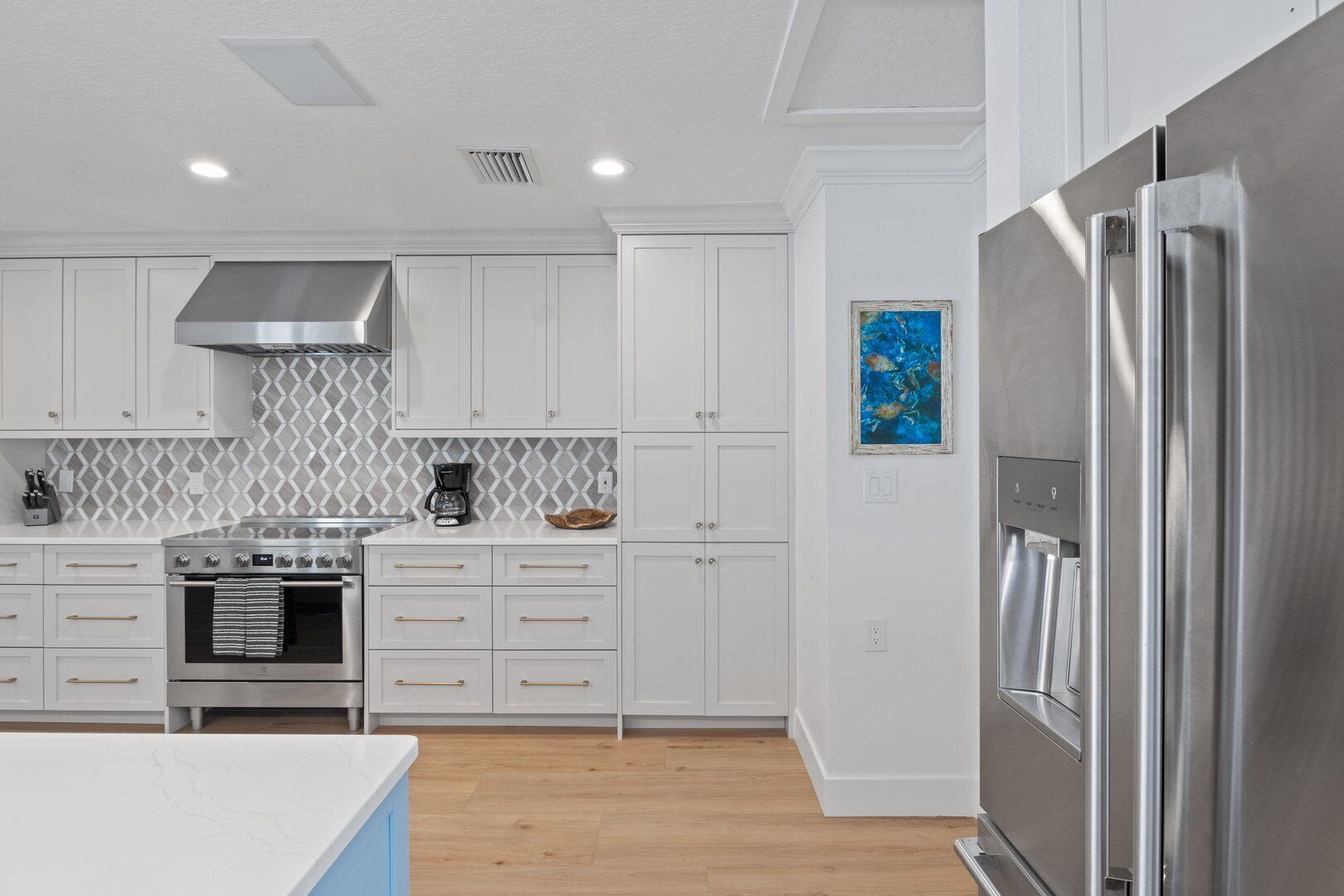 A modern kitchen with white cabinetry, a stainless steel range, a built-in oven, and a refrigerator.